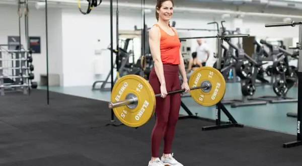 Tjej redo för marklyft startvikt med en skivstång med 15 kg vikter på varje sida.