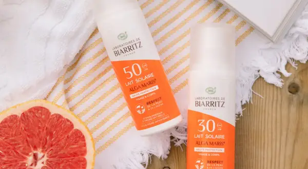 Två solkrämer från Biarritz med naturliga ingredienser, en med SPF 50 och en med SPF 30, ligger bredvid en grapefrukt och en bok.
