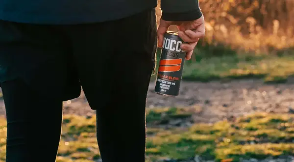 Person in athletic wear holding a NOCCO FOCUS energy drink can outdoors.