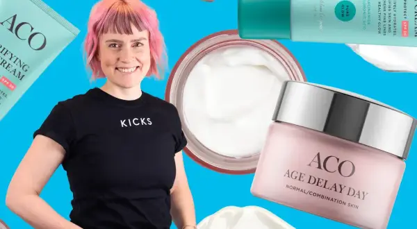 En kvinna med rosa hår ler omgiven av ACO-produkter, inklusive ACO ansiktskräm anti age.