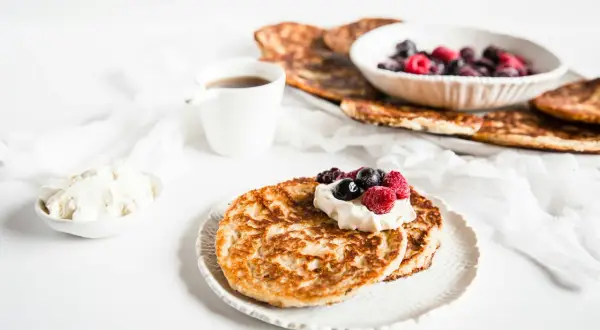 En härlig keto diet frukost med pannkakor, grädde och bär. En kopp kaffe står bredvid.