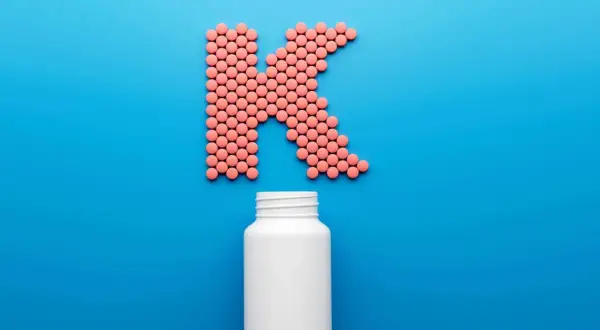 Rosa piller formar bokstaven K, med en tom vit burk nedanför. Kan det finnas k2-vitamin biverkningar?