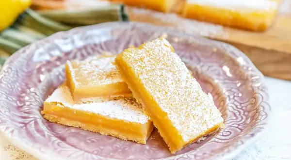 Citronkaka i långpanna, pudrad med florsocker, serveras på en vacker lila tallrik. Perfekt för fikat!