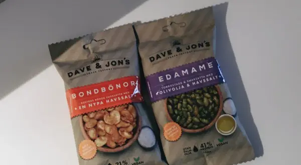 Två påsar Dave & Jon's snacks: Bondbönor och Edamame. Edamame-påsen visar torrostade edamamebönor med olivolja och havssalt.