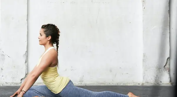 Kvinna i duvan yoga-position mot en sliten vägg.
