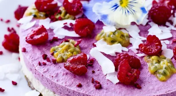 En vacker, lila tårta toppad med hallon, passionsfrukt och kokosflingor. En delikat och nyttig kaka som ser lika god ut som den smakar.