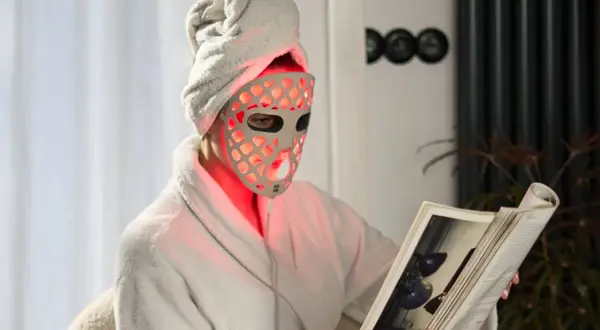 Person med handduk på huvudet och en led mask ansikte läser en bok i en morgonrock.
