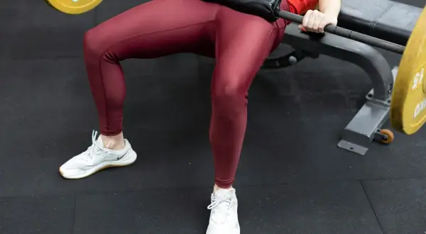 En person utför hip thrust med en skivstång på en bänk.