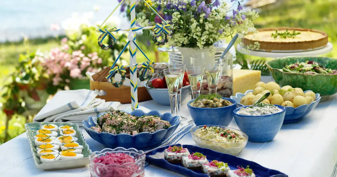 En härlig midsommar buffe med sill, potatis, ägg och en paj. En midsommarstång i bakgrunden.