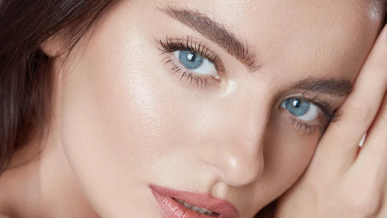 Närbild på en kvinna med blå ögon och perfekt makeup. Hennes ögonbryn ger en illusion av ett "brow lift".