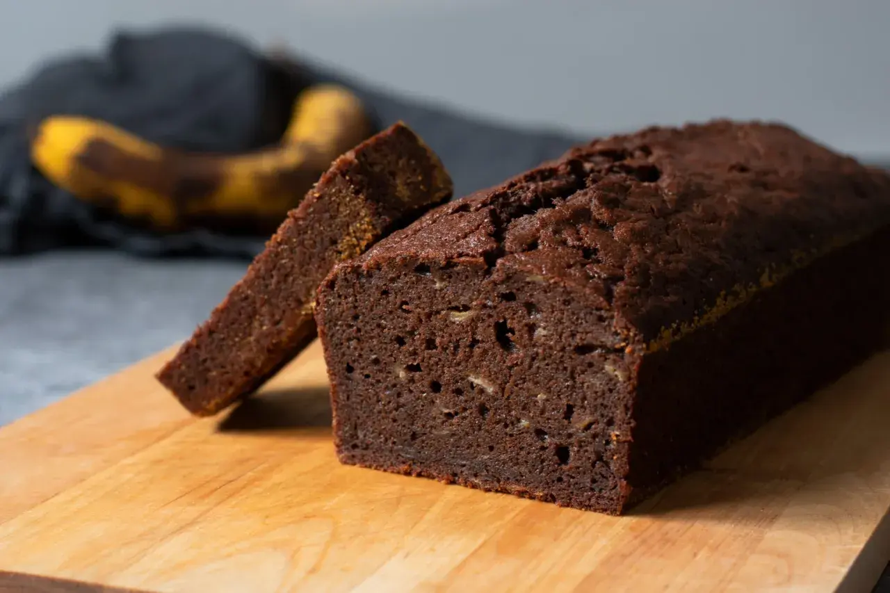 En saftig banankaka i långpanna, med en skiva uppskuren. En övermogen banan ligger i bakgrunden.