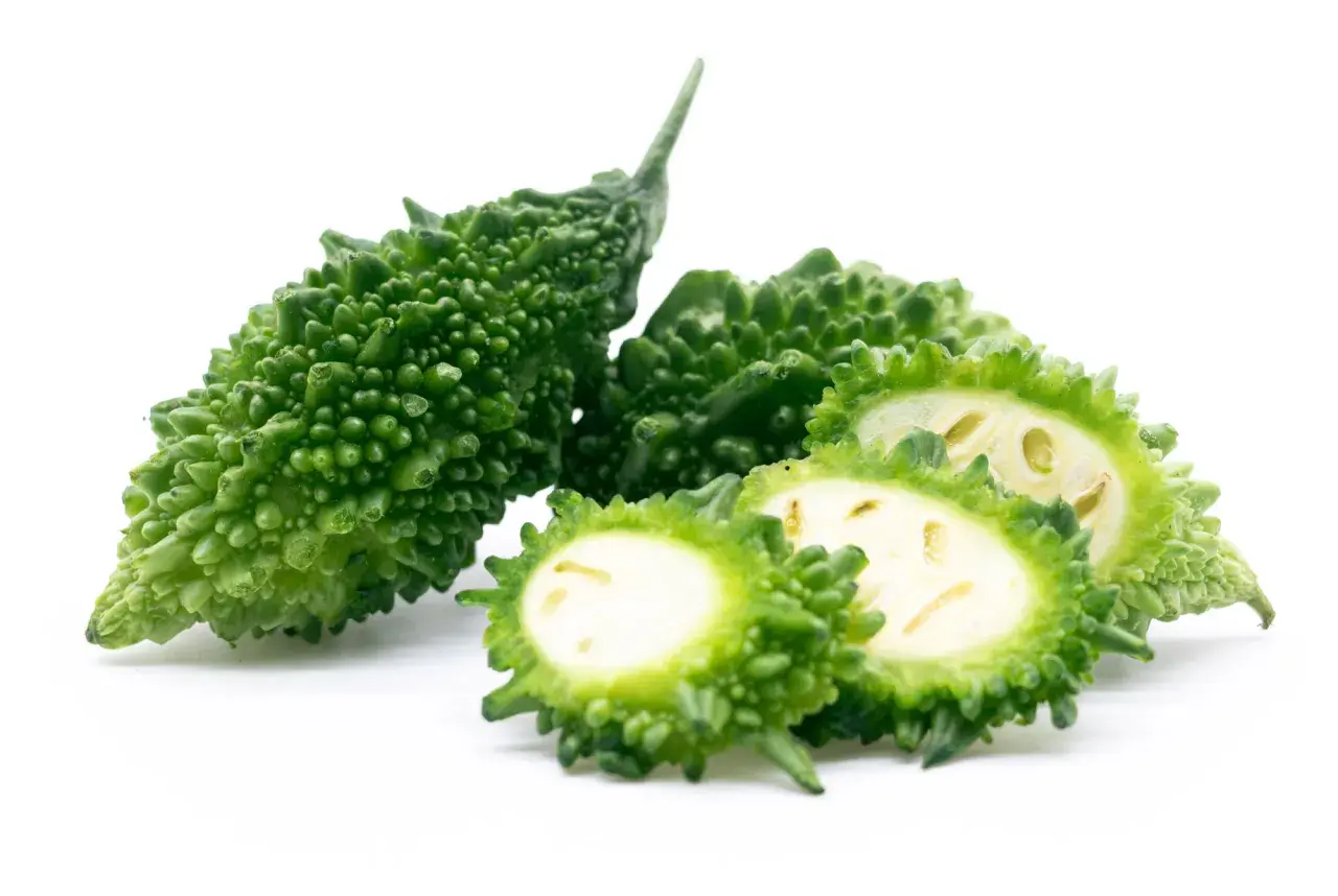 Gröna, taggiga bitter melonfrukter, en hel och några skivade, visar sitt ljusa inre.