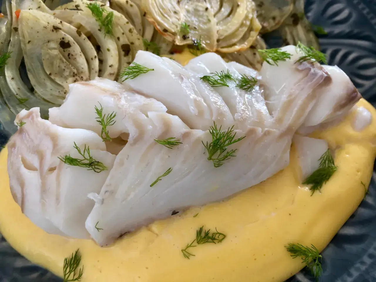 Läckert vit fisk serverad med krämig sås och ugnsbakad fänkål, garnerad med dill.