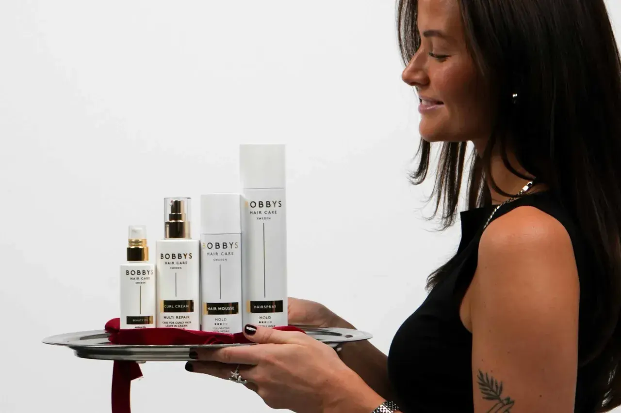 En kvinna presenterar en bricka med Bobby's Hair Care-produkter, inklusive Bobby's Curl Cream, för perfekt lockigt hår.