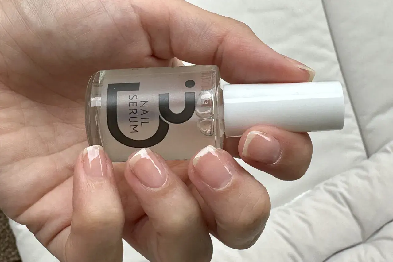 En hand håller en flaska nagelserum. Naglarna ser friska och starkare ut efter användning.