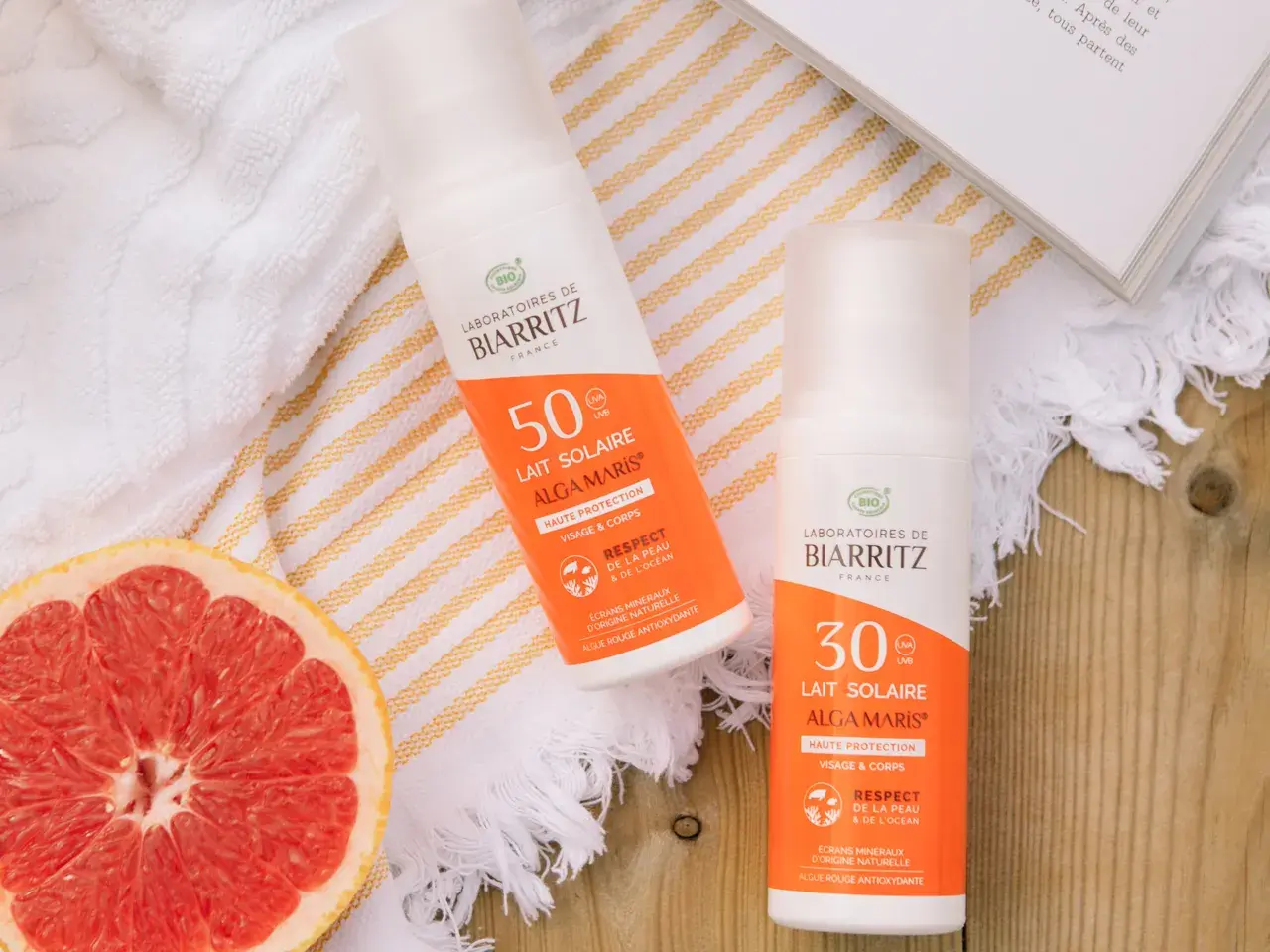 Två solkrämer från Biarritz med naturliga ingredienser, en med SPF 50 och en med SPF 30, ligger bredvid en grapefrukt och en bok.