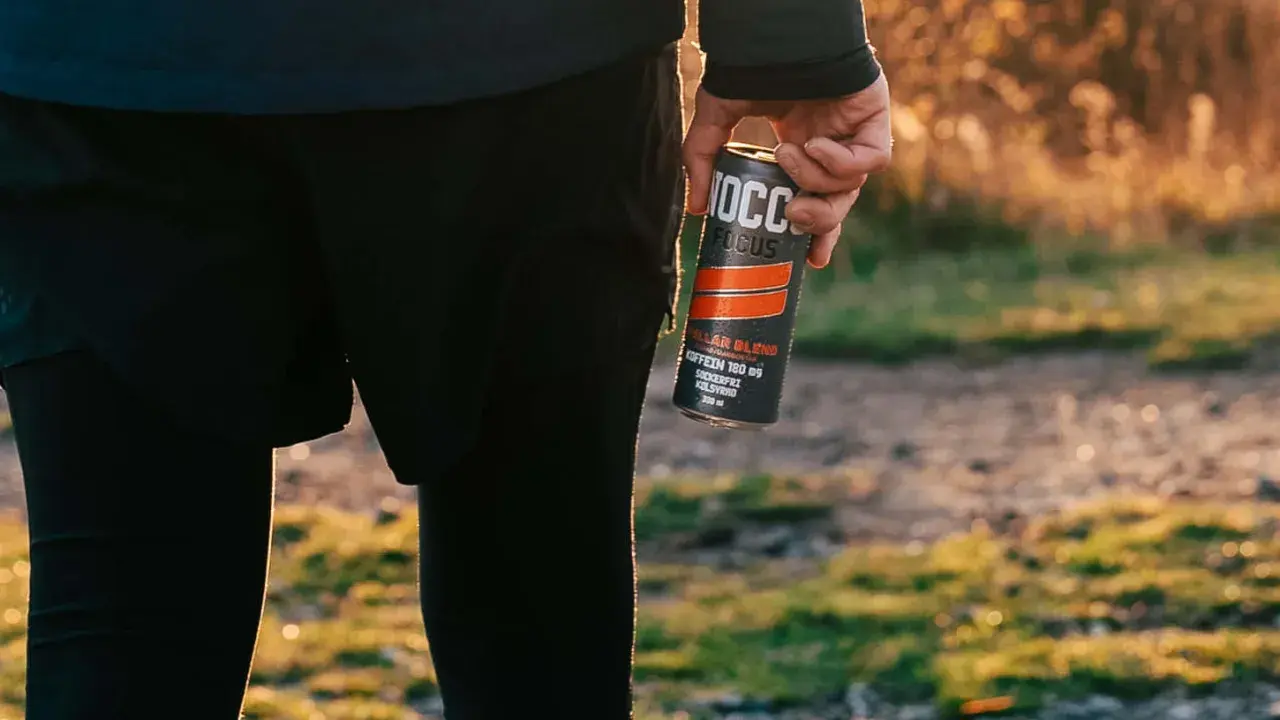 Person in athletic wear holding a NOCCO FOCUS energy drink can outdoors.