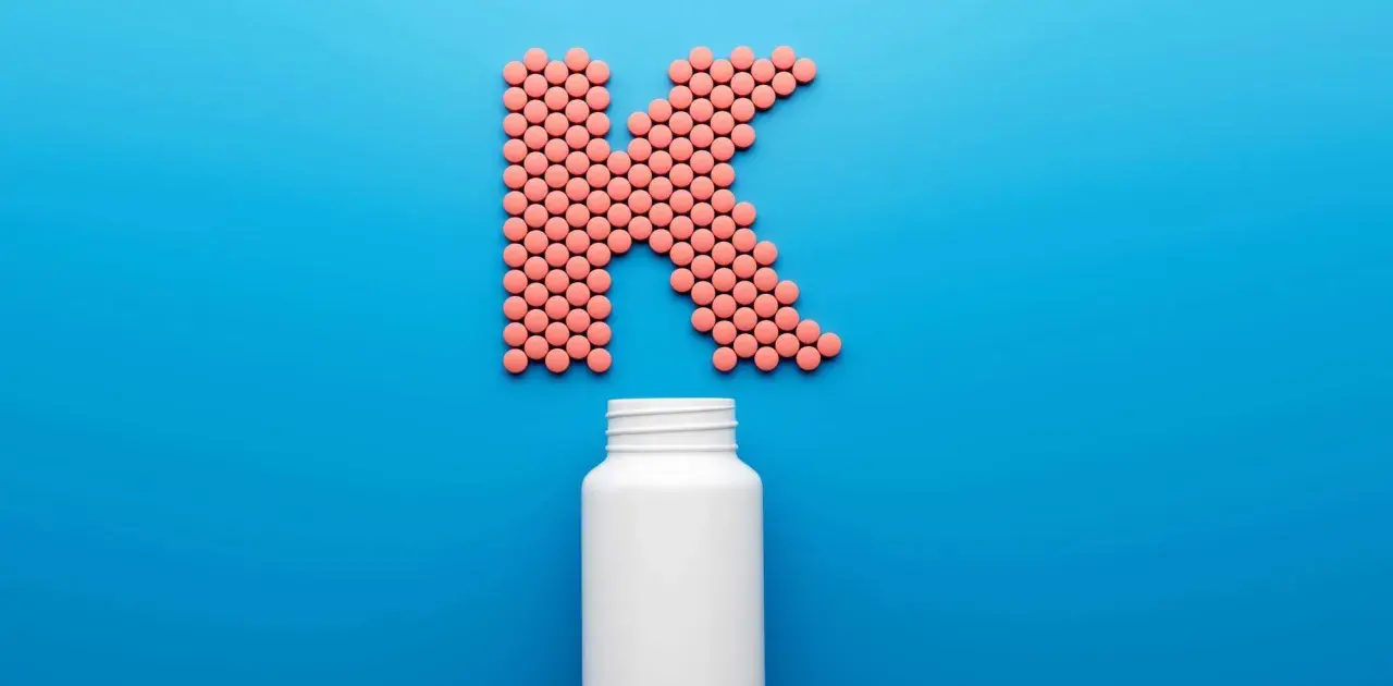 Rosa piller formar bokstaven K, med en tom vit burk nedanför. Kan det finnas k2-vitamin biverkningar?