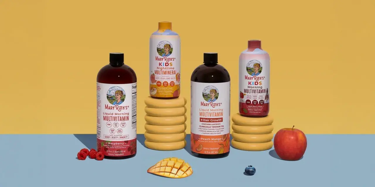 Flera flaskor Mary Ruths multivitamin i olika smaker, inklusive barnvarianten. Frukt som hallon, mango och äpple finns bredvid.