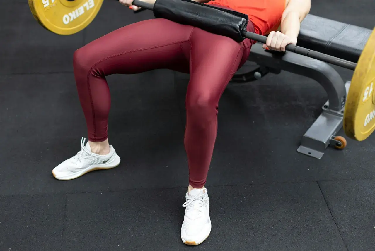 En person utför hip thrust med en skivstång på en bänk.