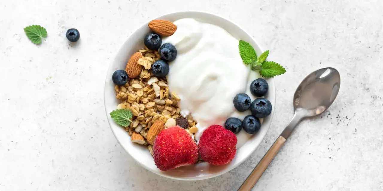 En skål med grekisk yoghurt, granola, blåbär, jordgubbar och mandlar. En nyttig och god frukost.