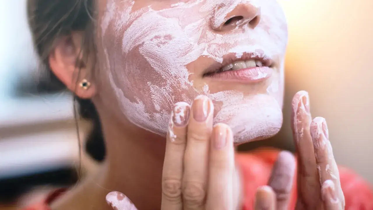 En kvinna applicerar en kr&auml;mig mask i ansiktet. Hennes fingrar, t&auml;ckta av produkten, sm&ouml;rjer in huden. Detta &auml;r en del av en rutin f&ouml;r probiotika hudv&aring;rd.