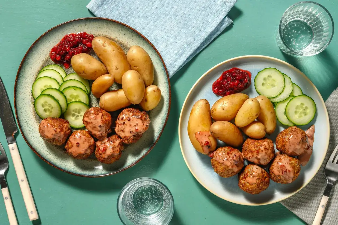 Två tallrikar med köttbullar, potatis, gurka och lingonsylt. En klassisk svensk comfort food-måltid.