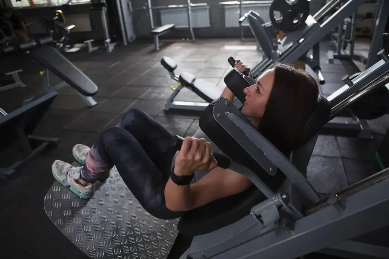 Kvinna tr&auml;nar ben p&aring; en hack squat-maskin i ett gym.