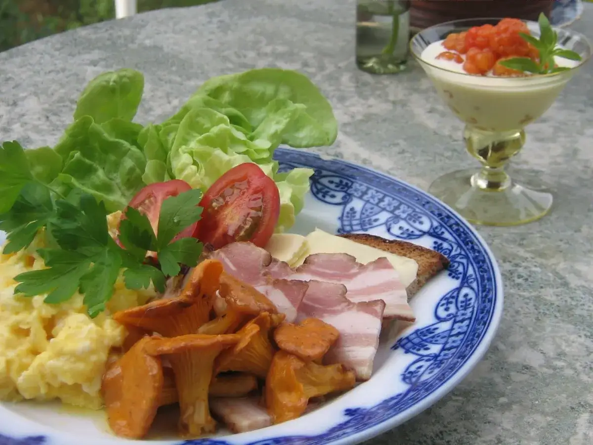 En h&auml;rlig brunch meny med &auml;ggr&ouml;ra, kantareller, bacon, ost, tomat och sallad. En dessert med hjortron i bakgrunden.