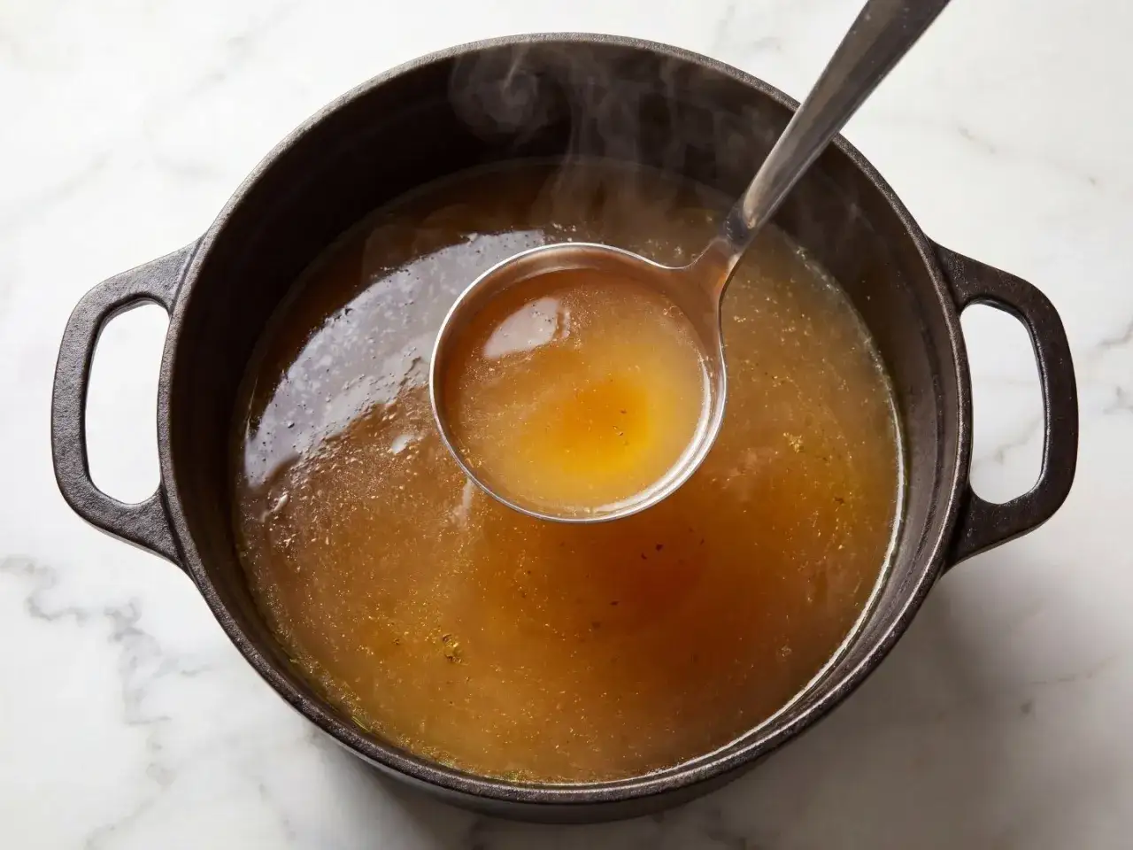 En slev lyfter gyllene buljong från en gjutjärnsgryta. Doften av real broth savory spices sprider sig.
