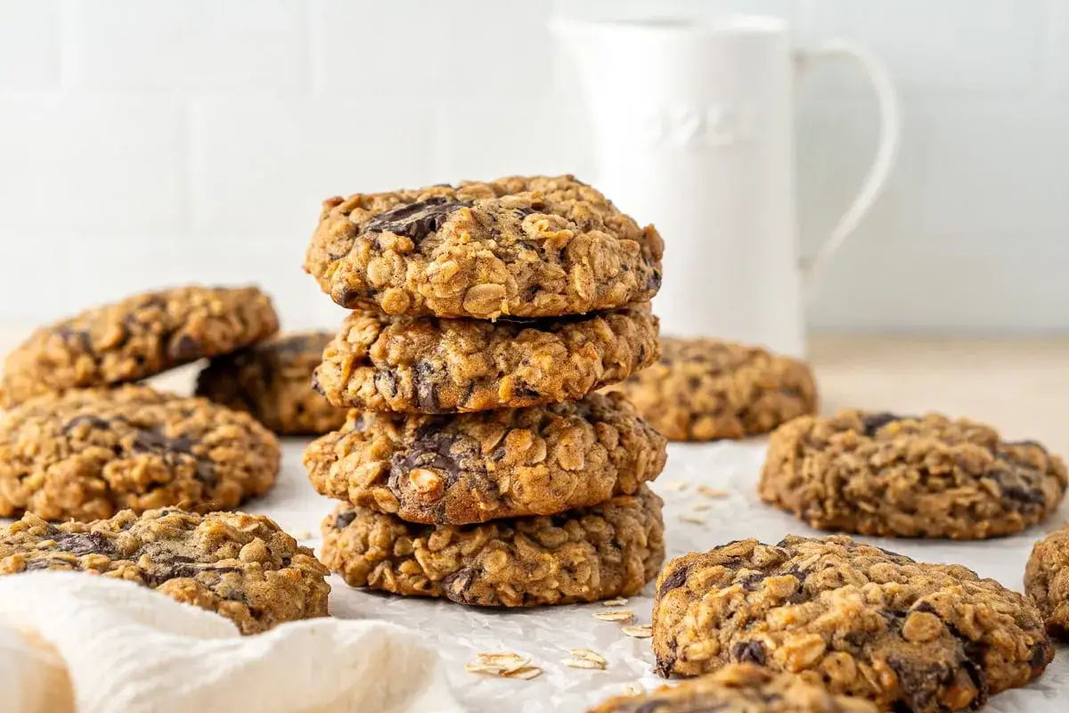 En h&ouml;g med nyttiga kakor med chokladbitar, omgivna av fler kakor och en vit kanna i bakgrunden.