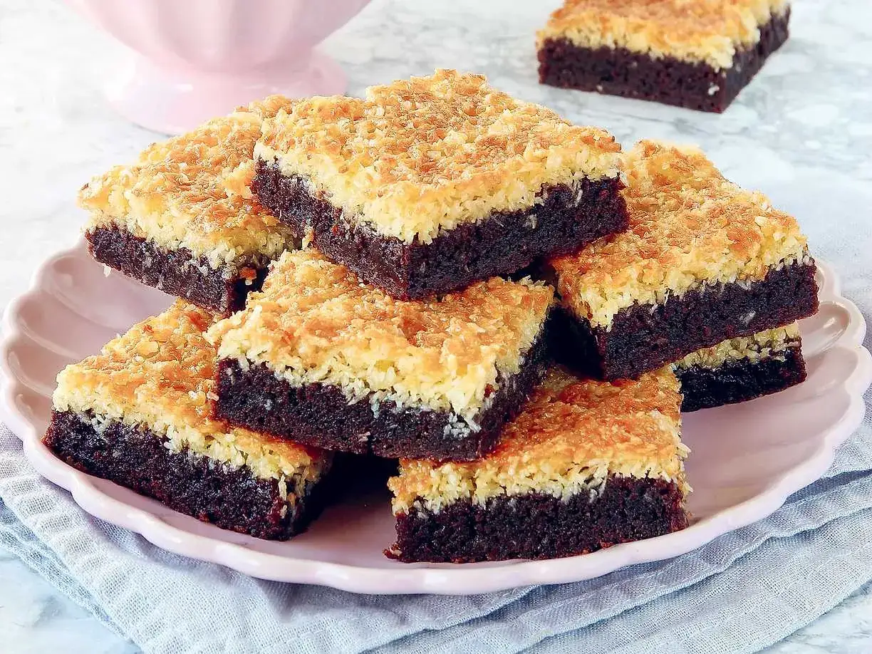 En h&ouml;g med kladdkaka med kokostosca p&aring; en rosa tallrik. Den m&ouml;rka chokladbottnen toppas med en gyllene, krispig kokosb&auml;dd.