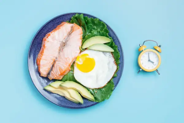Tallrik med lax, ägg och avokado bredvid en väckarklocka. Dags för fasta 24 timmar.