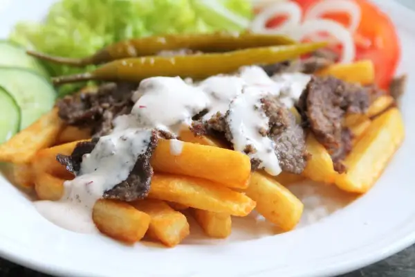 En tallrik med pommes frites, kebabkött, vit sås, sallad, gurka, tomat, lök och inlagda paprikor. Ett perfekt kebab recept för en snabb middag.