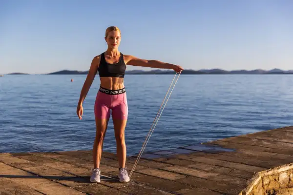 En kvinna utför face pulls med ett träningsband vid havet.