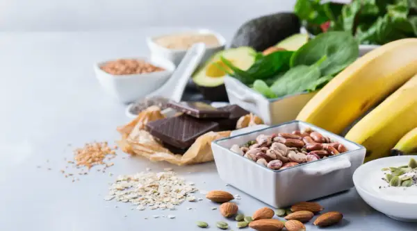 En härlig samling av magnesiumrik mat: bönor, mandlar, mörk choklad, bananer, spenat, avokado och frön.