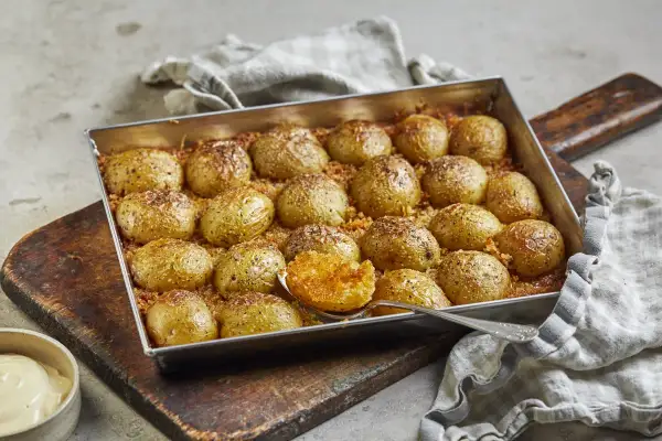 Ugnsbakade potatishalvor, gyllene och kryddade, redo att serveras. En sked visar den mjuka insidan av en perfekt rostad potatis.