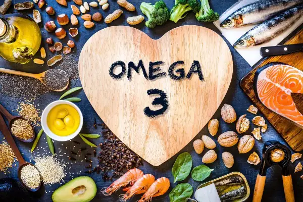 En hjärtformad träskiva med texten "OMEGA 3" omgiven av lax, sardiner, räkor, nötter, frön, broccoli och olivolja. En hälsosam måltid!