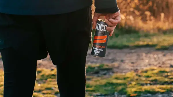 Person in athletic wear holding a NOCCO FOCUS energy drink can outdoors.