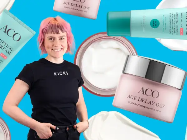 En kvinna med rosa hår ler omgiven av ACO-produkter, inklusive ACO ansiktskräm anti age.