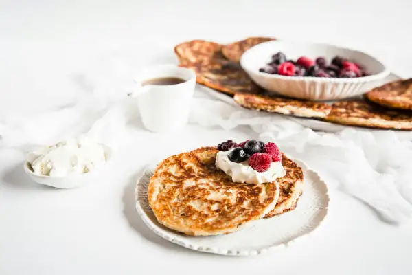 En härlig keto diet frukost med pannkakor, grädde och bär. En kopp kaffe står bredvid.