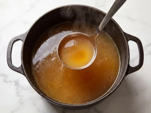 En slev lyfter gyllene, ångande buljong från en gjutjärnsgryta. Doften av real broth savory spices sprider sig.